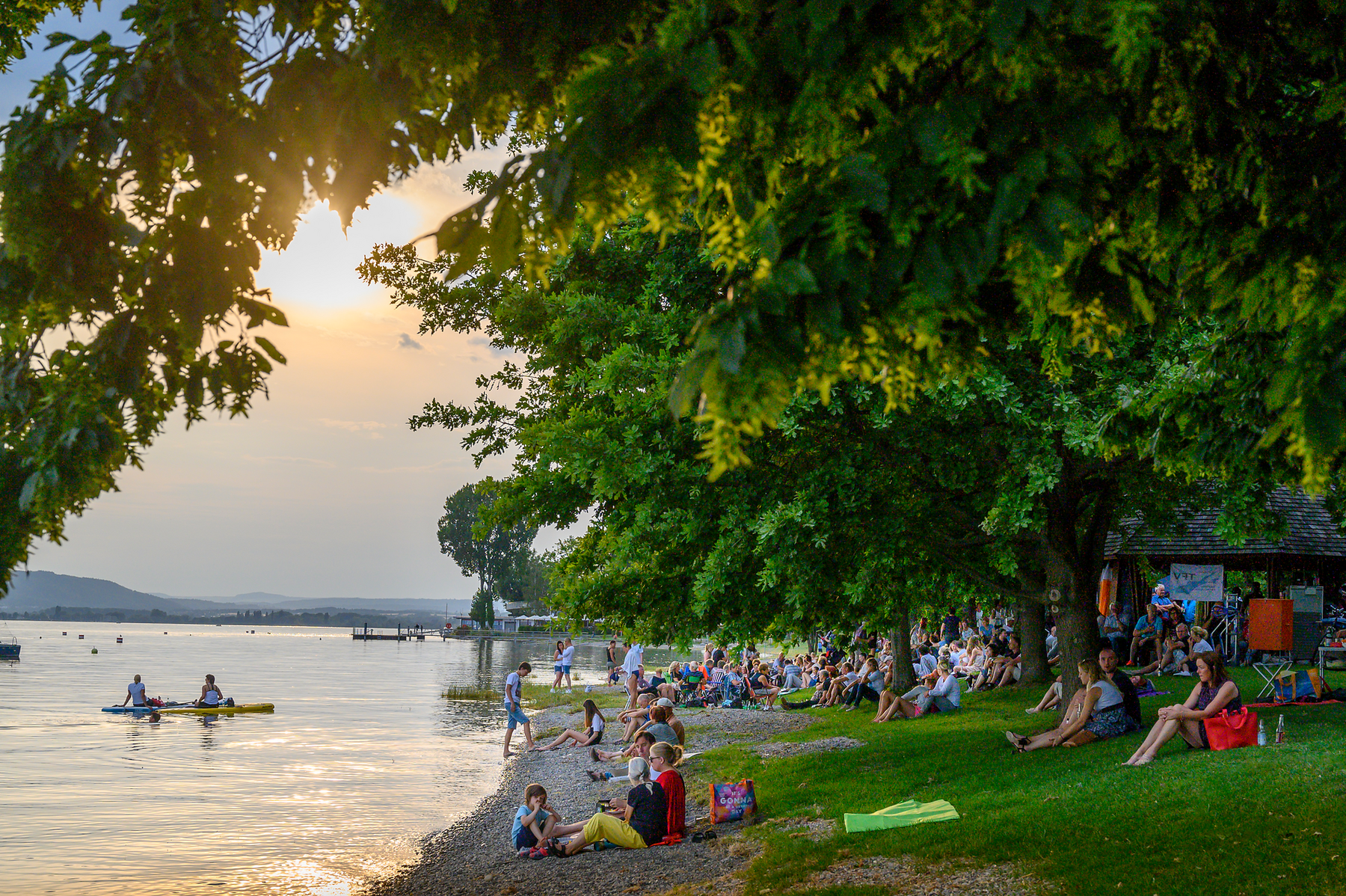 Menschen betrachten den Sonnenuntergang am Bodenseeufer Menschen betrachten den Sonnenuntergang am Bodenseeufer