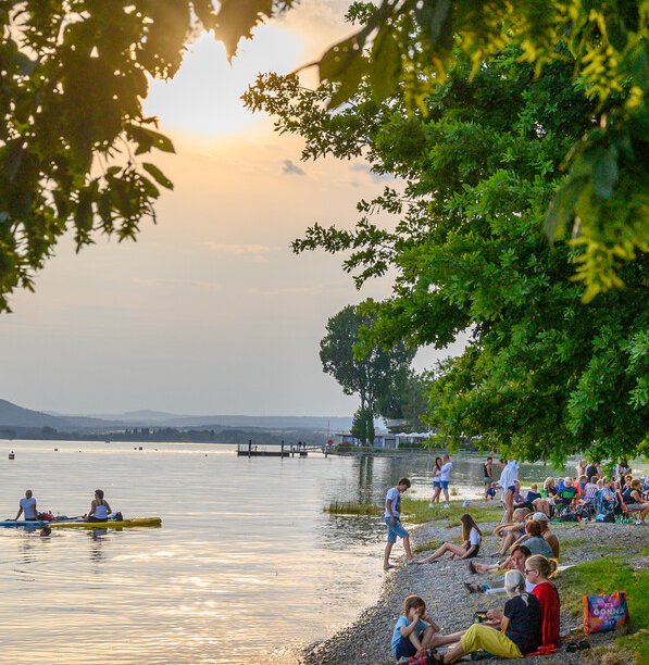 Menschen betrachten den Sonnenuntergang am Bodenseeufer Menschen betrachten den Sonnenuntergang am Bodenseeufer