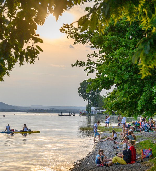 Menschen betrachten den Sonnenuntergang am Bodenseeufer